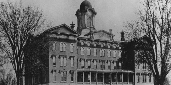 Black and white image of a historical building (Old Main) with a clock tower and arched windows.