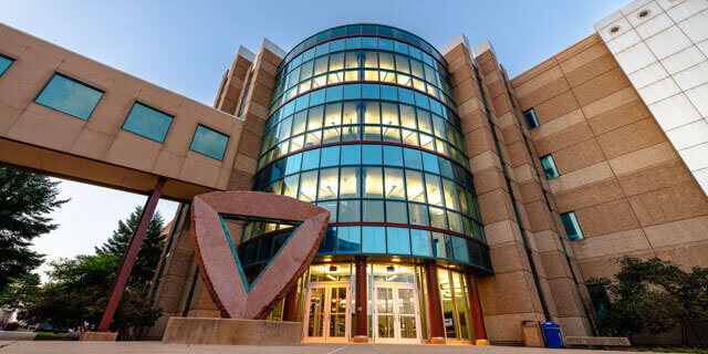 A building with a semi-circular glass facade and a triangular sculpture near the entrance.
