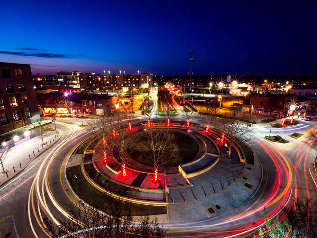 Aerial view of a city roundabout at night with red lights and dynamic vehicle light trails.