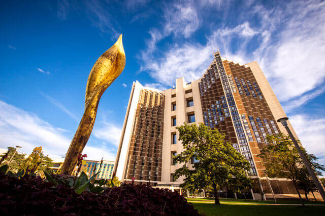 A modern building with unique architecture and a golden sculpture in front, under a vibrant blue sky.