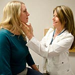 Female physician assistant checking the neck glands of a female patient.