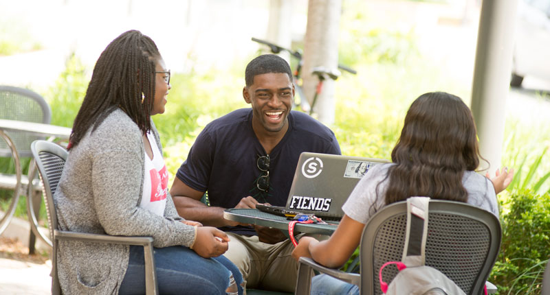 Three students chat at a table outside the Coffee Hound.